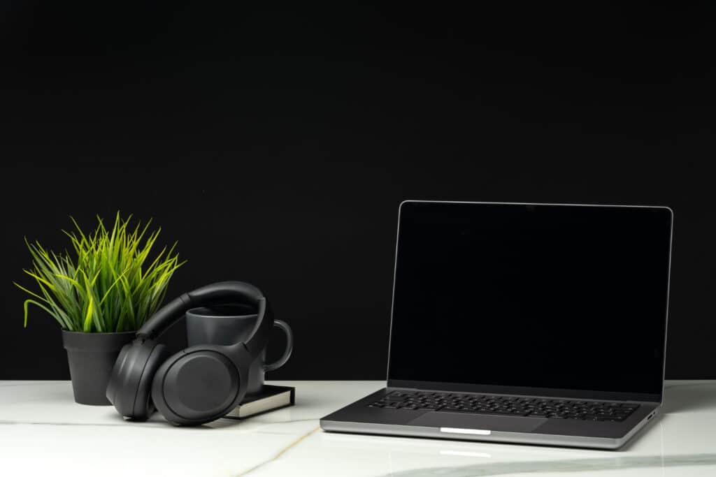 Portátil en un escritorio junto a unos auriculares, una taza y una planta
